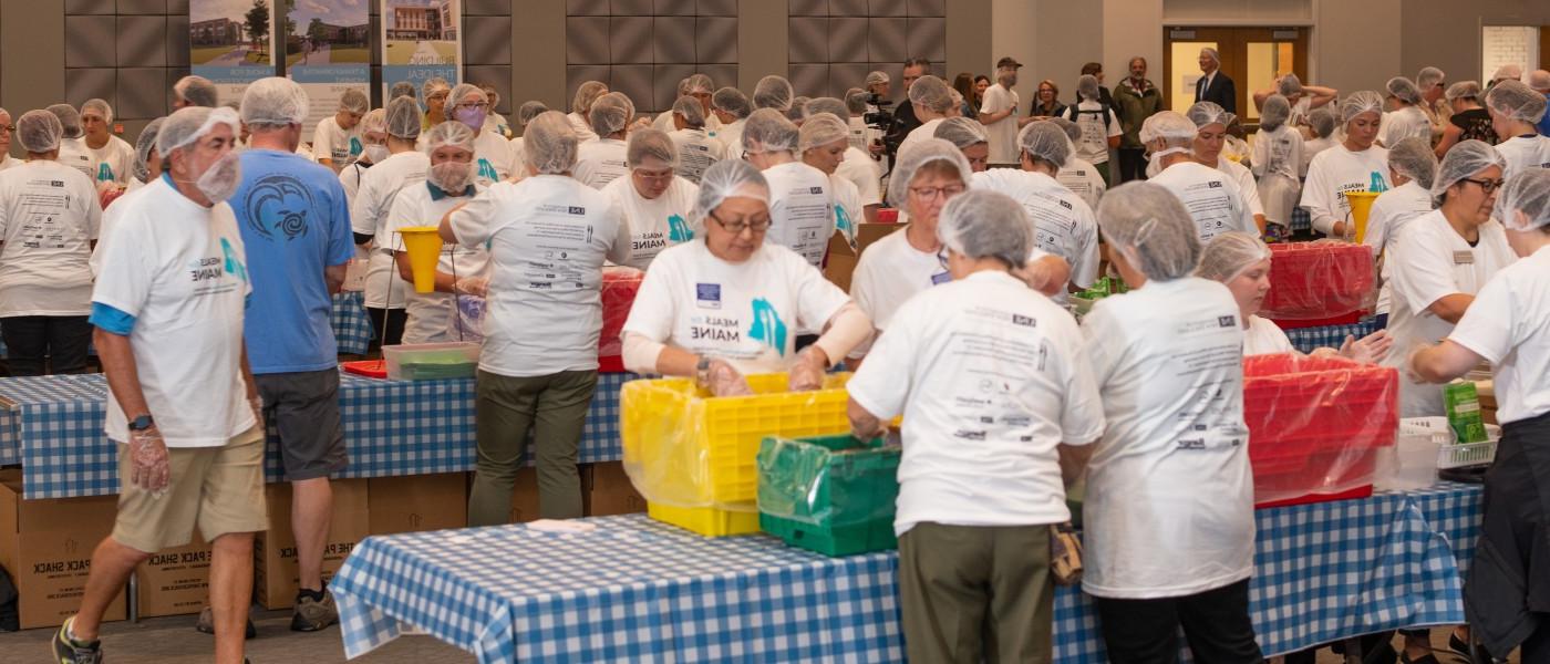 A room filled with 缅因州美食 volunteers working to pack meals